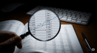 A magnifying glass focusing on a financial ledger, illustrating the importance of internal controls and vigilant oversight for preventing employee wire fraud in small businesses.